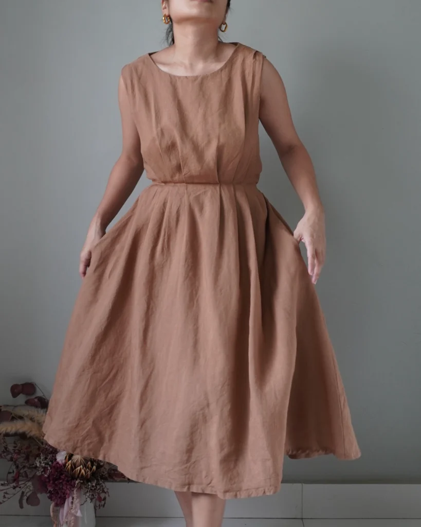 Timeless cocoa sleeveless dress with pleat details, has a ribbon that ties to the back, pleat details, flowy finish